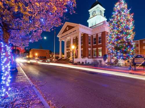 A festive town square at night, featuring a decorated Christmas tree and a historic building illuminated with lights.