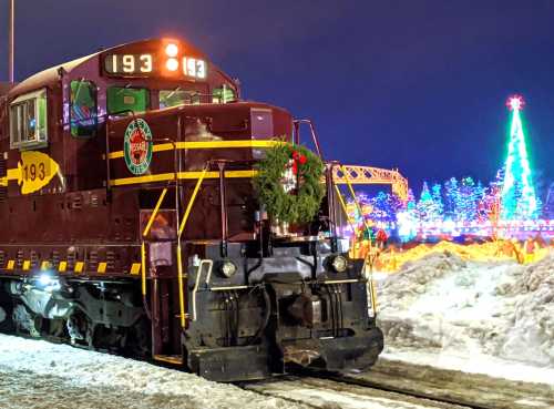 A festive train with a wreath on the front, surrounded by colorful holiday lights and snow.