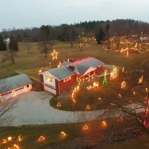 Aerial view of a house decorated with colorful Christmas lights and festive displays in a spacious yard.