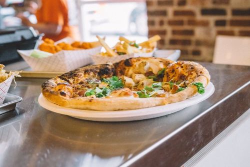 A freshly baked pizza topped with herbs on a white plate, sitting on a counter with other food in the background.