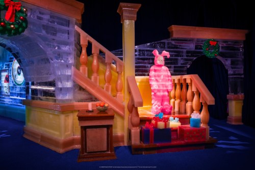 A colorful ice sculpture of a figure stands on a staircase, surrounded by festive decorations and presents.