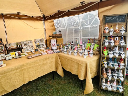 A craft market stall featuring various handmade items, including gnomes, decorations, and art pieces on display.