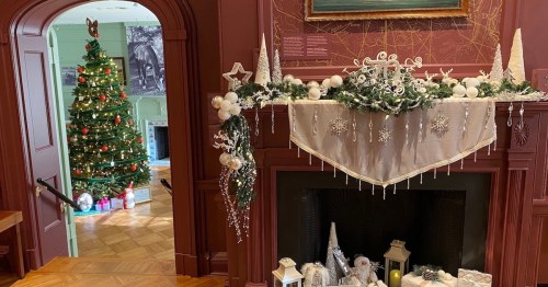 A cozy room decorated for the holidays, featuring a Christmas tree and festive mantel decor with snowflakes and candles.