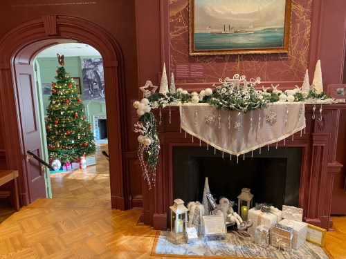 A cozy room decorated for the holidays, featuring a Christmas tree and a festive mantel with ornaments and gifts.