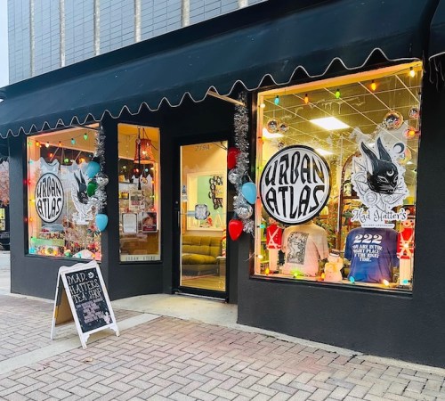 A storefront with "Urban Atlas" signage, colorful decorations, and a chalkboard sign outside.