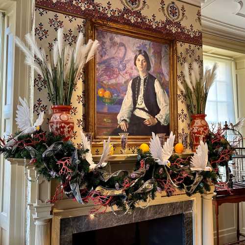 A decorated mantel with greenery and ornaments, featuring a portrait of a woman in a vintage frame above it.