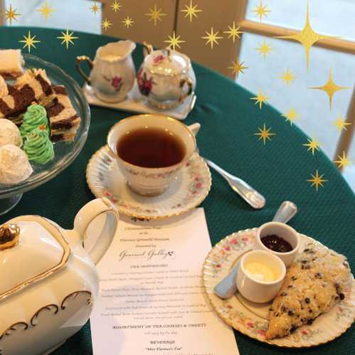 A tea setting with a teapot, cups, assorted sweets, and a menu on a green tablecloth, surrounded by decorative stars.