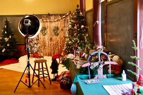 A festive room decorated with Christmas trees, lights, and holiday props, featuring a photography setup.