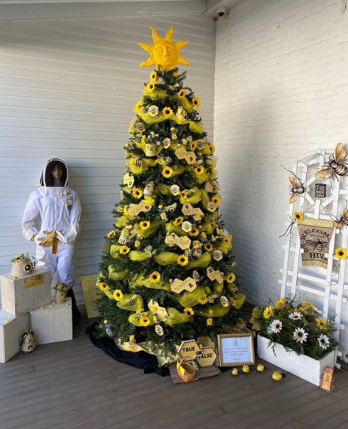 A yellow-themed Christmas tree adorned with sunflowers, bees, and a sun topper, surrounded by decorative elements.