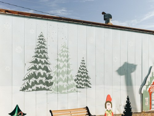A mural of snowy trees on a wall, with a bench in front and a shadow of a building in the background.