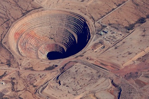 Aerial view of a large, circular open-pit mine surrounded by arid land and small structures.