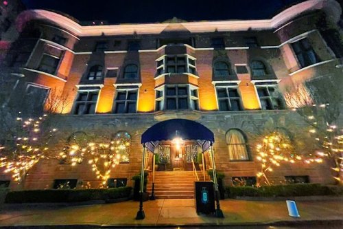 A beautifully lit brick building at night, adorned with warm lights and a blue awning at the entrance.