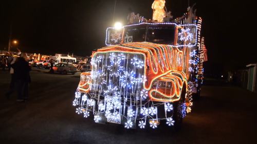 A brightly lit truck adorned with colorful lights and snowflake decorations at night, surrounded by people.