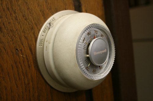 Close-up of a vintage Honeywell thermostat mounted on a wooden wall, displaying temperature settings.