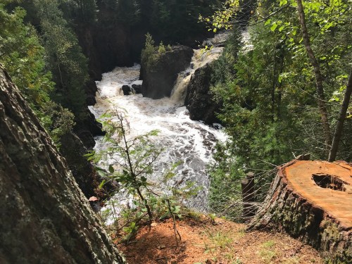 A scenic view of a waterfall cascading through a forest, surrounded by lush greenery and rocky cliffs.
