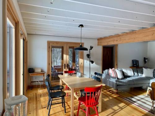 Bright, modern living space with a wooden dining table, red chairs, a gray sofa, and large windows letting in natural light.