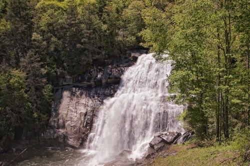 A cascading waterfall surrounded by lush green trees and rocky terrain in a serene natural setting.
