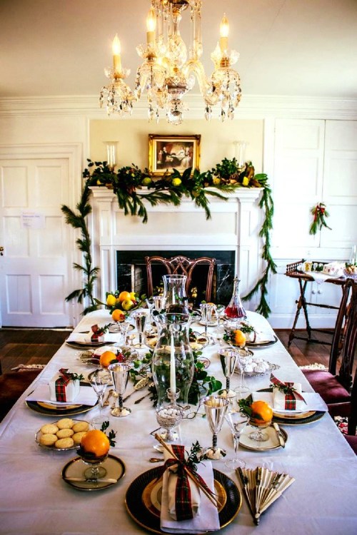 Elegant dining table set for a festive meal, adorned with greenery, candles, and decorative plates.