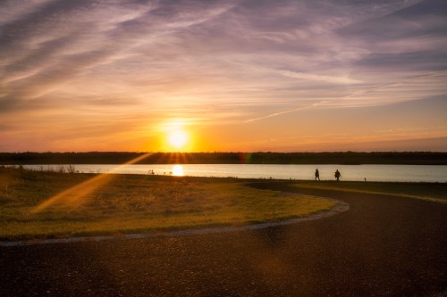 A serene sunset over a lake, with two people walking along a winding path beside the water.