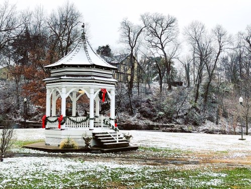 A white gazebo decorated with red ribbons, surrounded by a snowy landscape and bare trees.