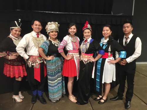 A group of eight people in traditional attire, smiling and posing together at a cultural event.