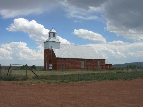 A rustic stone church with a white roof, set against a cloudy sky and grassy landscape.