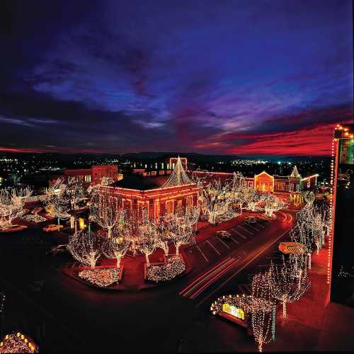 A vibrant sunset over a town square adorned with festive holiday lights and illuminated trees.