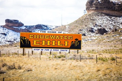 Sign for Chugwater Chili, inviting visitors to stop for a free taste, set against a snowy landscape.