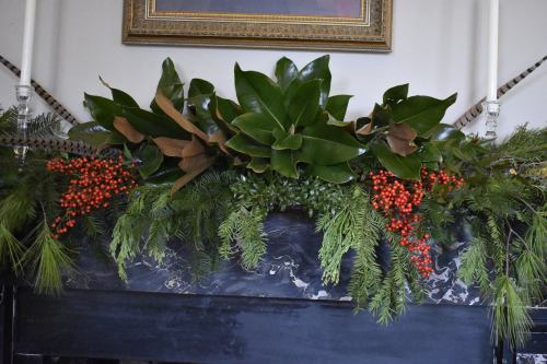 A festive mantel arrangement featuring greenery, magnolia leaves, and red berries.