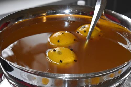 A silver bowl filled with a brown liquid containing three whole lemons and spices.