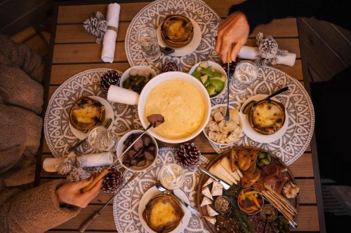 A cozy table setting with fondue, bread, and assorted snacks, surrounded by festive decorations and drinks.