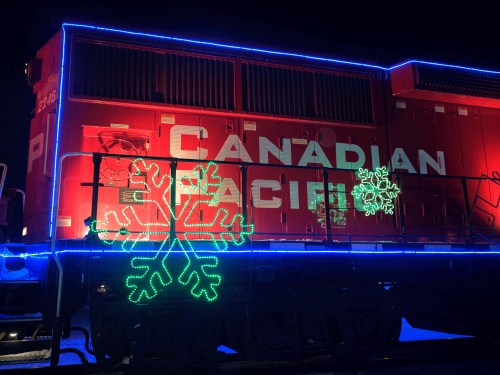 A brightly lit Canadian Pacific train decorated with colorful snowflake lights for the holiday season at night.