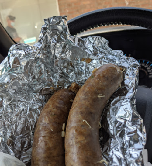 Two sausages wrapped in foil, resting on the dashboard of a car.