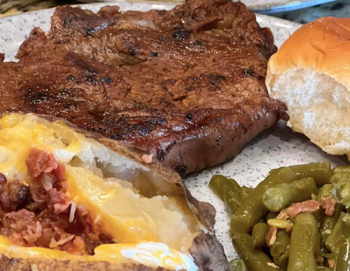 A plate featuring a grilled steak, baked potato with toppings, green beans, and a soft dinner roll.