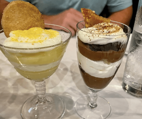 Two dessert glasses: one with lemon mousse and a cookie, the other with chocolate mousse and whipped cream, garnished.