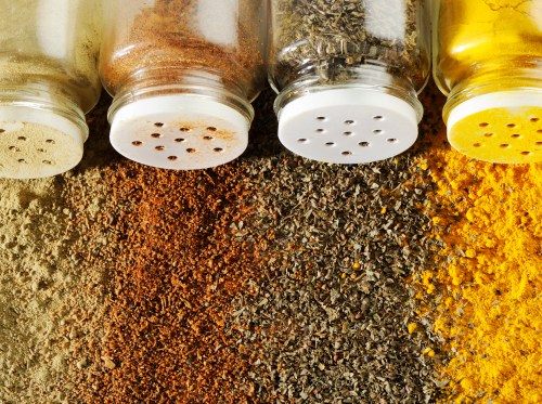 Four spice jars filled with various colorful spices and herbs arranged in a row on a textured surface.