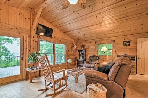 Cozy wooden cabin interior with a seating area, large windows, and a view of nature. Warm lighting and rustic decor.