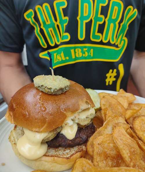 A close-up of a burger with pickles and sauce, served with crispy potato chips on the side.