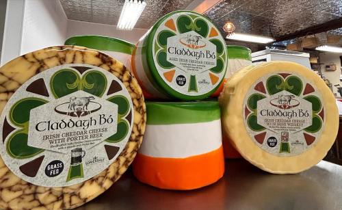 A stack of Claddagh Bó cheese wheels, featuring Irish cheddar with porter beer and aged cheddar, in vibrant colors.