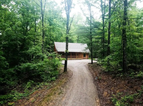 A cozy cabin nestled in a lush green forest, accessed by a gravel path.
