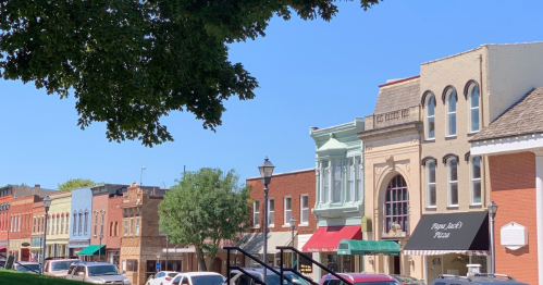 A charming street lined with historic buildings, shops, and trees under a clear blue sky.