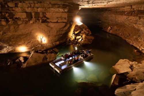 A boat with passengers navigates a dimly lit cave, surrounded by rocky walls and calm water.