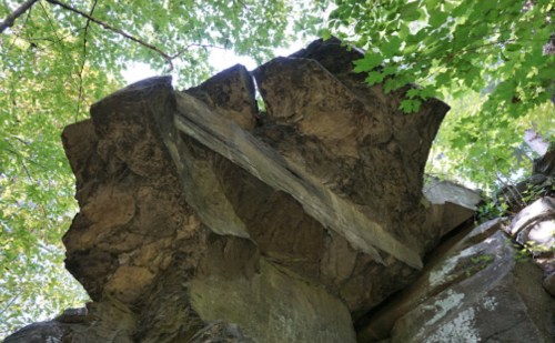 A large rock formation with a wooden beam resting on top, surrounded by green foliage and trees.