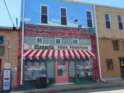 A colorful mural of a vintage soda fountain shop with a striped awning, featuring ice cream and hot dogs.