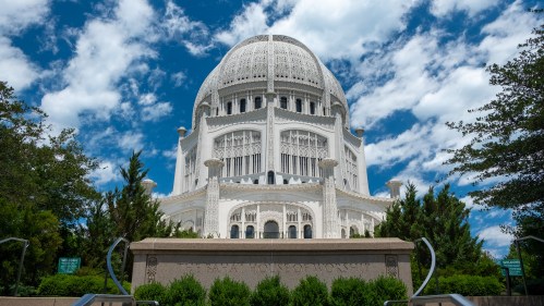A large, ornate white building with a dome, surrounded by greenery and under a blue sky with clouds.