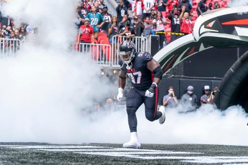 A football player runs onto the field through smoke, with a cheering crowd in the background.