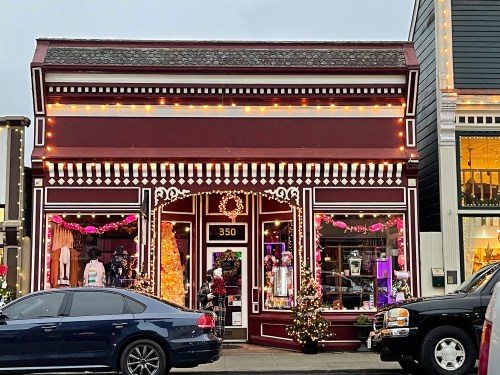 A festive storefront decorated with lights and holiday decor, featuring a large window display and a Christmas tree.