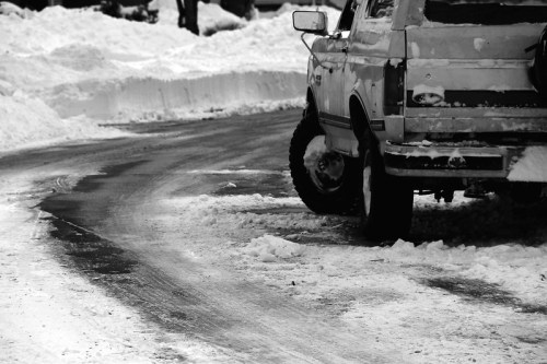 A snowy road curves around a parked truck, with snowbanks lining the sides. The scene is in black and white.