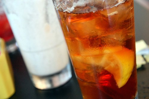 A glass of iced tea with lemon slices, featuring ice cubes, in a casual dining setting.