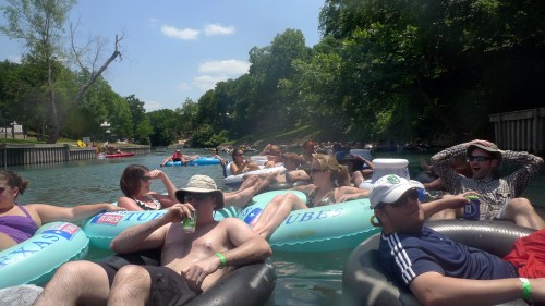A group of people relaxing on inner tubes in a river, surrounded by trees and enjoying a sunny day.